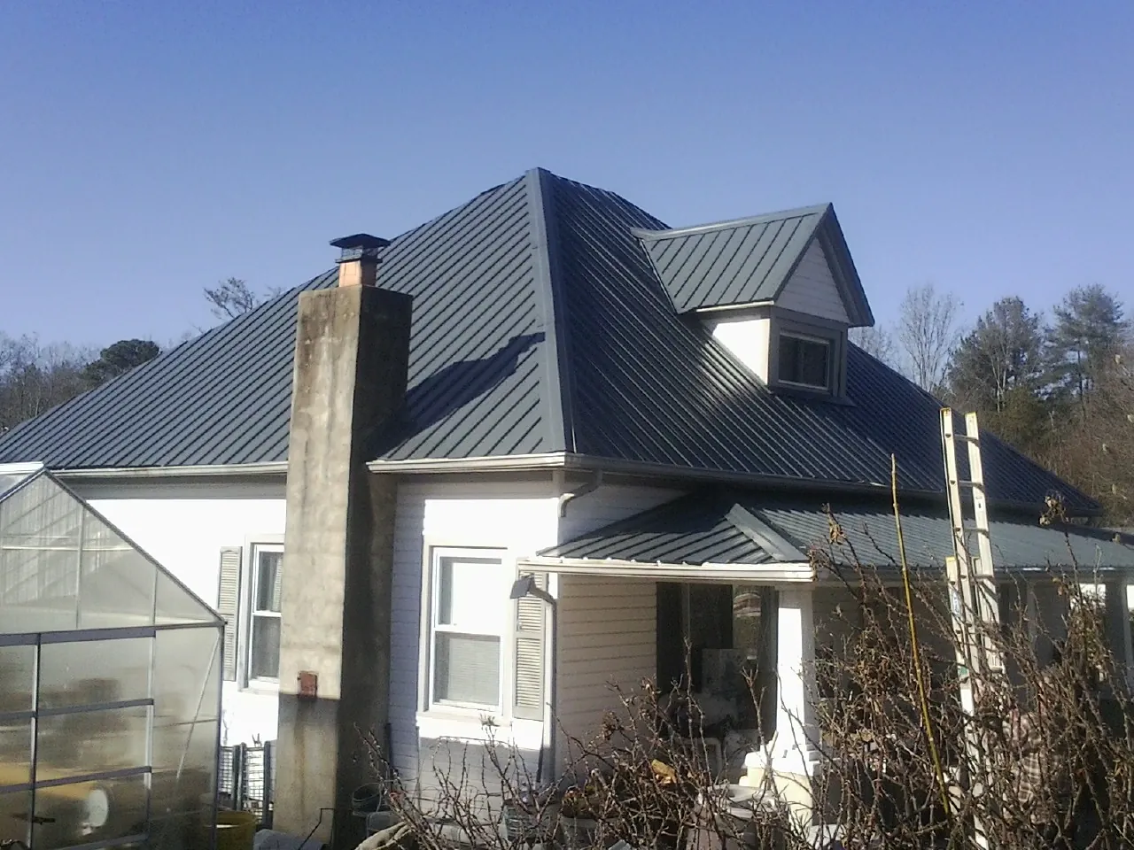 Dark blue standing seam metal roof on a white farmhouse with dormer — Slate & Tile Roof Repair by Roofing Brothers in Aquasco