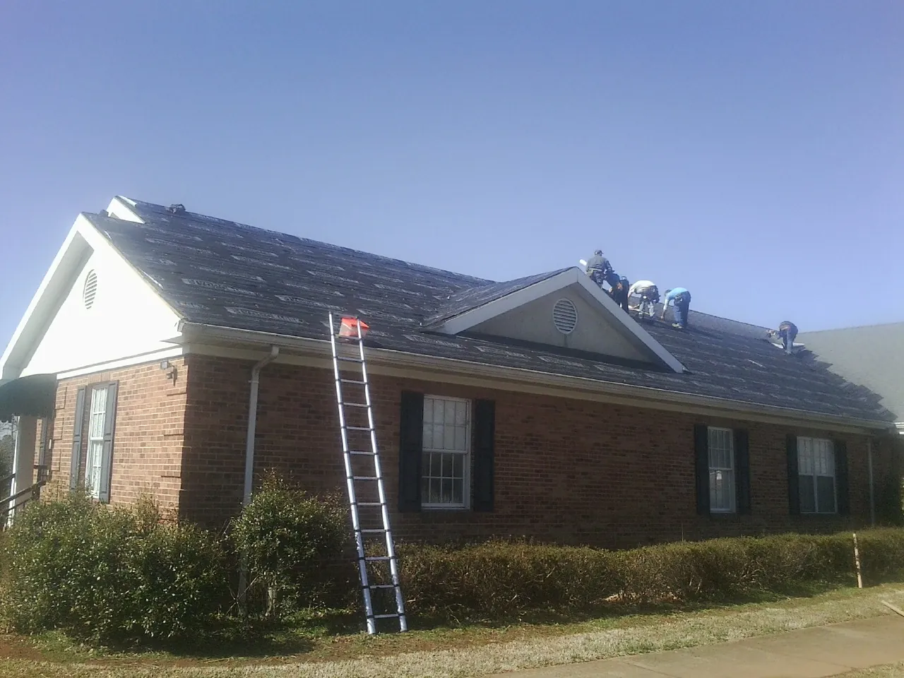 Crew tearing shingles off a brick ranch roof with a ladder set — Emergency Roof Repair work by our crew in Aquasco