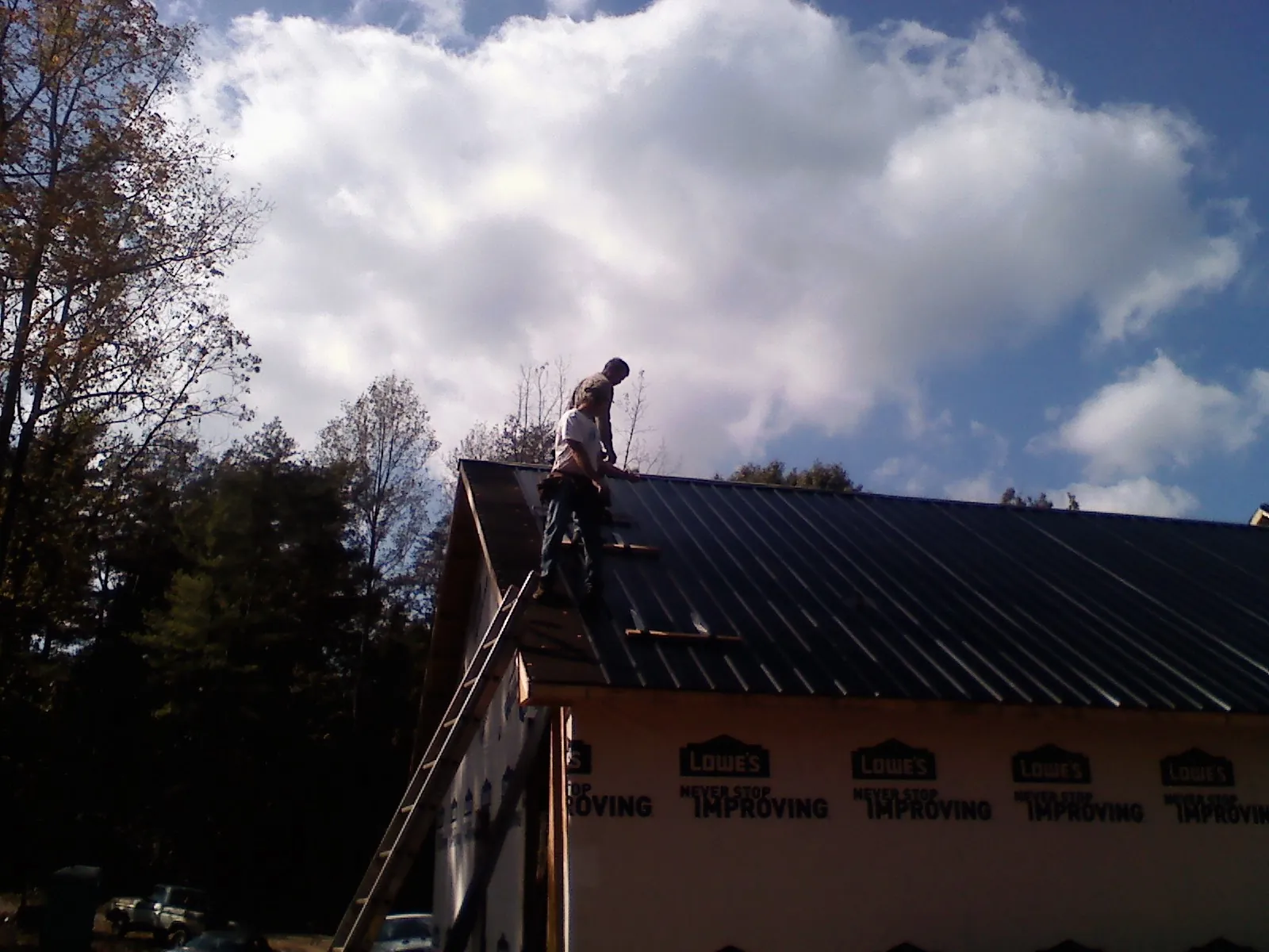 Roofer fastening dark metal panels high against a cloudy sky, from a Roof Inspection job in Aquasco