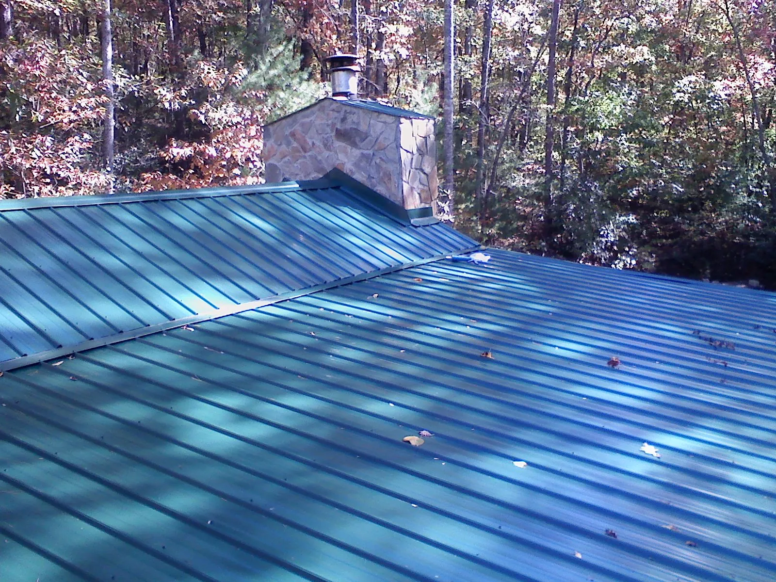 New green metal roof and stone chimney surrounded by autumn woods in Aquasco