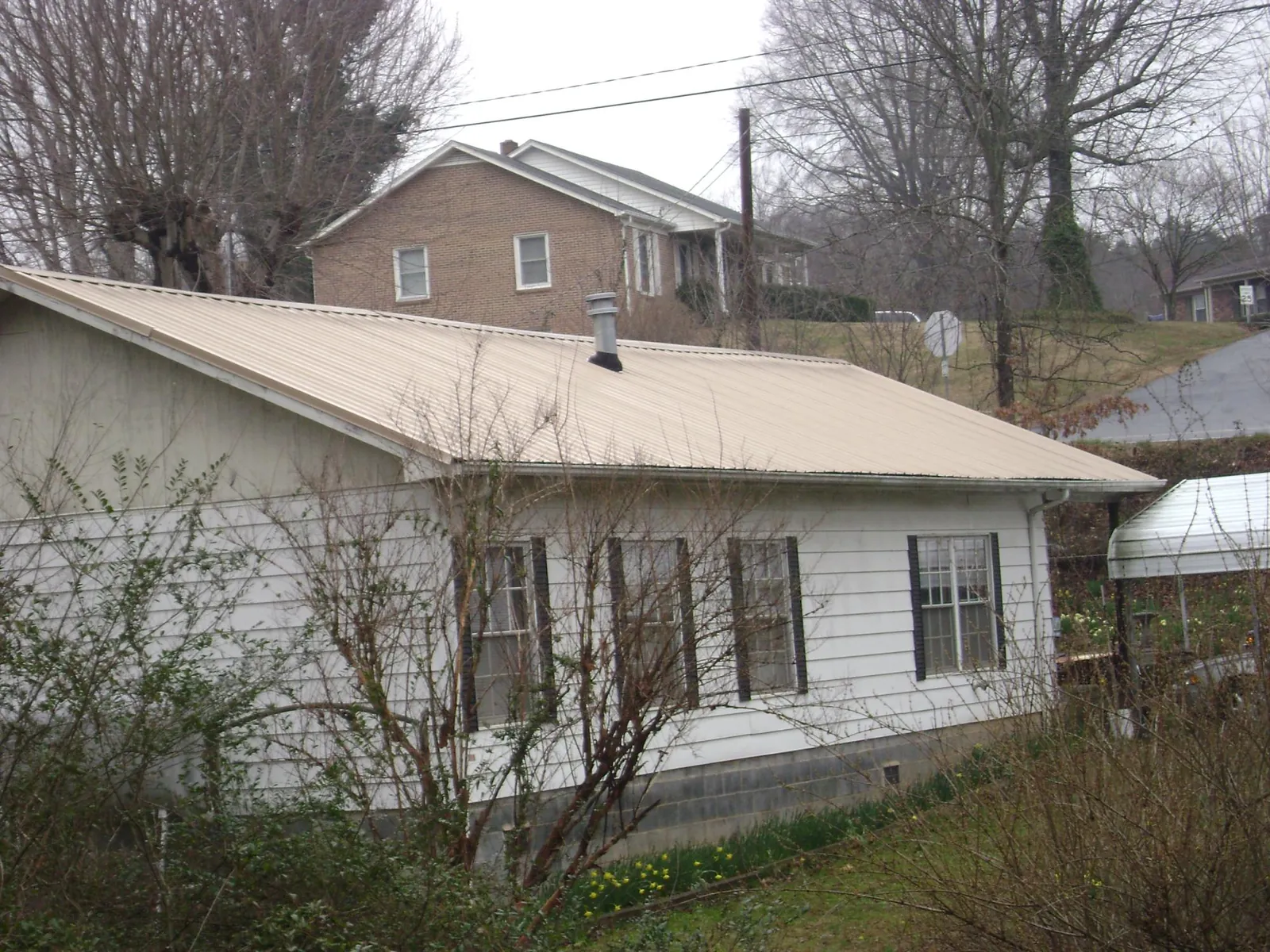 Tan metal roof on a white sided house set into a hillside — Commercial Roofing by Roofing Brothers in Aquasco